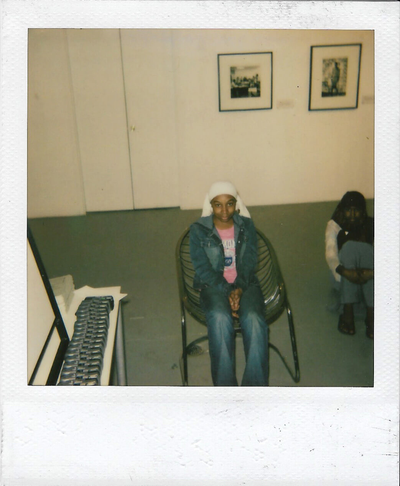 Polaroid snapshot of two young women in an art gallery. One is seated in a chair and one is on the floor